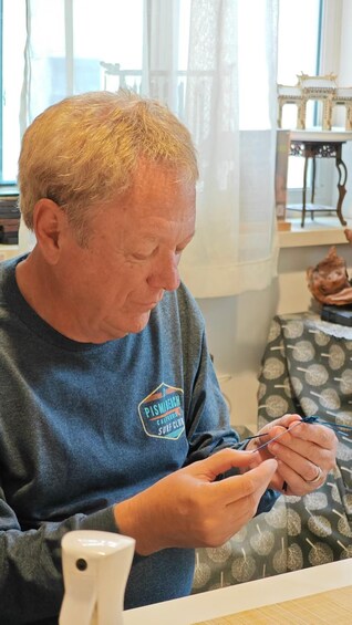 A person wearing a Pismo Beach Surf Club sweatshirt, sitting indoors and holding a smartphone. 4