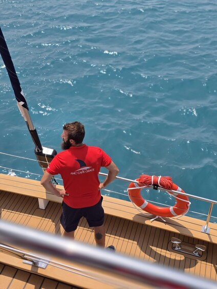 A person on a boat wearing a red shirt with "AMC CAPE GRACE" on the back, looking at the water. 3