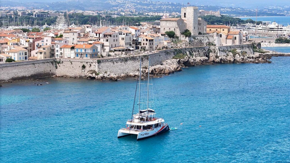 A coastal town with a historic castle, a marina with boats, and a clear blue sea. 5