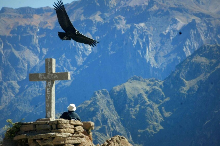 A person sitting on a stone structure with a cross sign in a mountainous area. 3