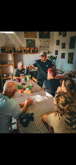 A group of people seated around a table with a patterned tablecloth, engaged in a meal. 4
