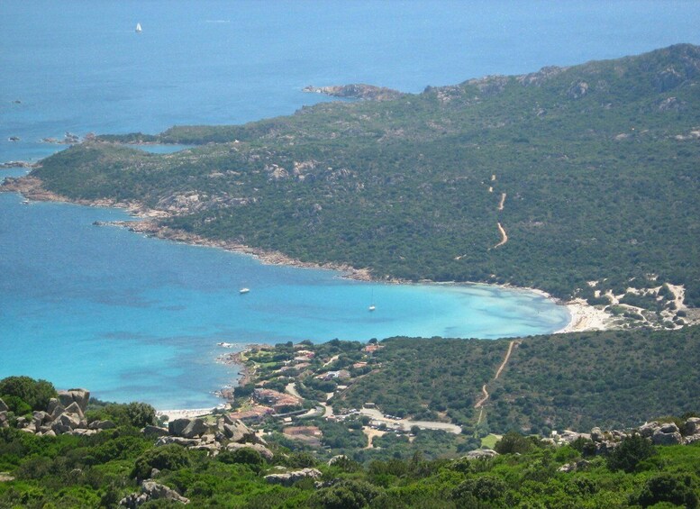 A coastal landscape with a clear blue sea, green hills, and a small village. 4