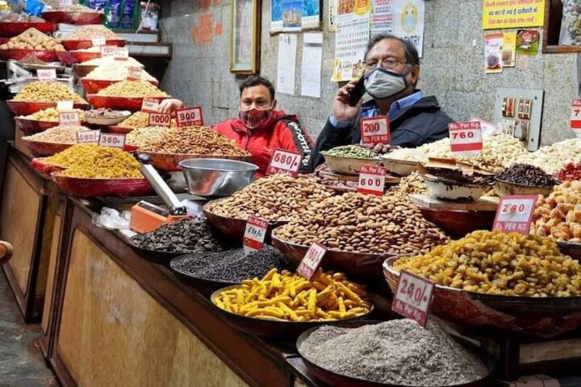 A market stall with various grains and legumes displayed in large bowls, each with a price tag. 1