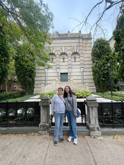 Two people standing in front of a historic building with intricate stonework and a decorative gate. 2