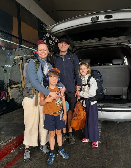A family with backpacks standing in front of a vehicle with an open trunk. 3