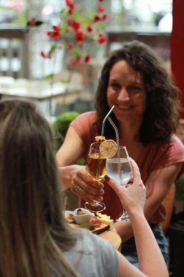 Two people toasting with drinks, one with a straw and a slice of orange in a glass, and the other with a straw in a glass of water. 1