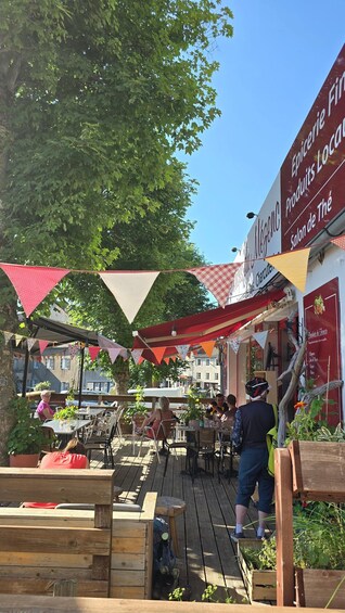 An outdoor café with wooden tables and chairs, red and white triangular flags, and a sign for 'Negoce'. 2