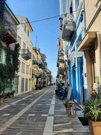 A narrow street lined with colorful buildings, a scooter parked on the side, and potted plants. 3
