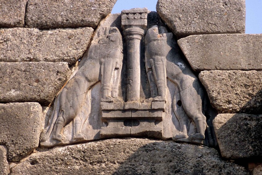 A stone relief of three figures standing on a platform, flanked by columns, set into a stone wall. 2