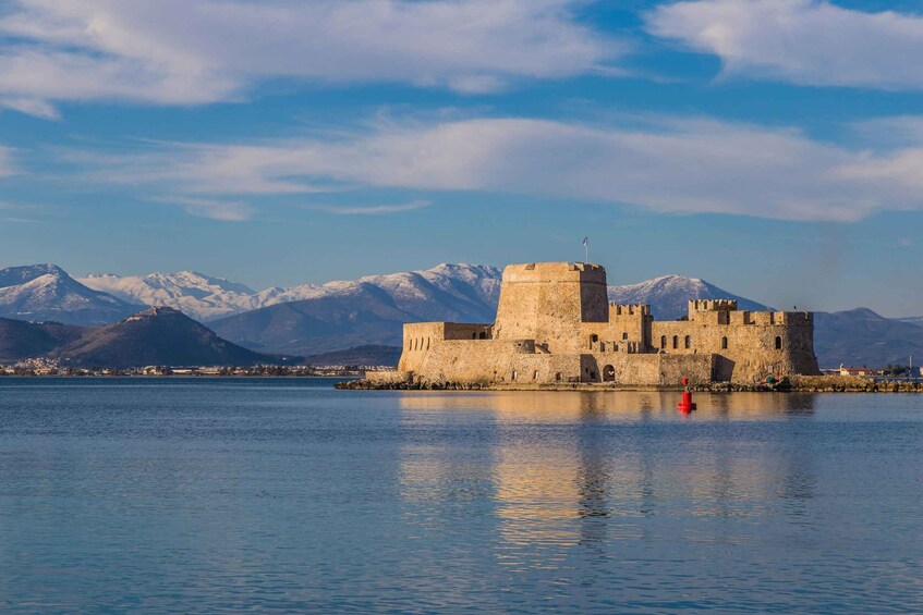 A historic stone castle by a calm lake with snow-capped mountains in the background. 1