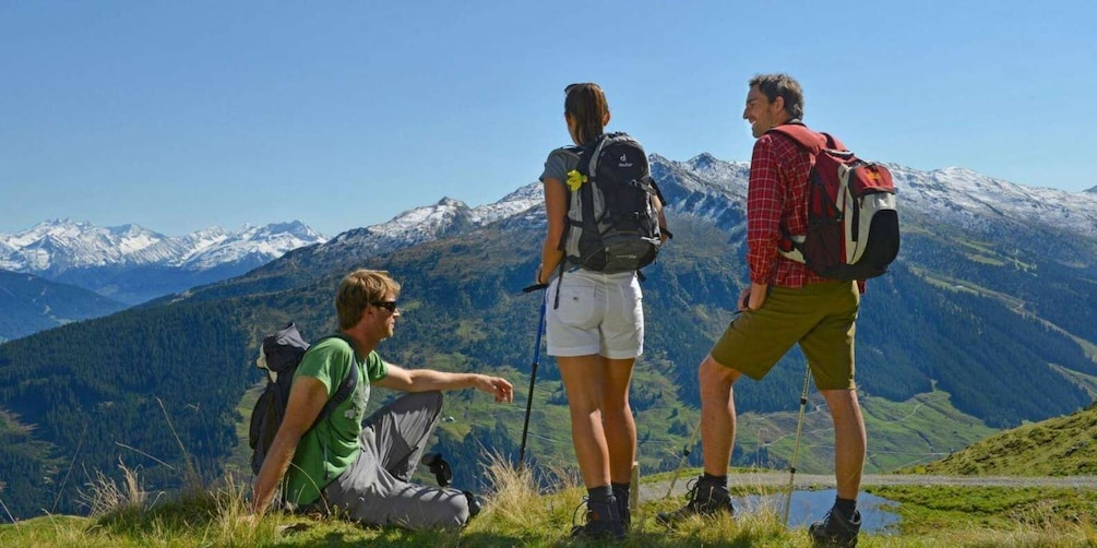 Three hikers on a mountain trail with snow-capped peaks in the background. 1