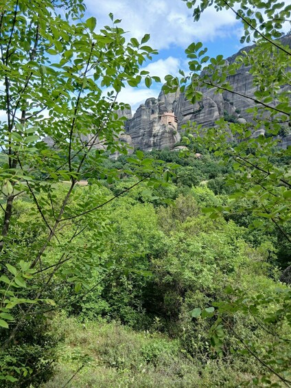 A lush green landscape with dense foliage in the foreground and a historic building perched atop a rocky cliff in the background. 2