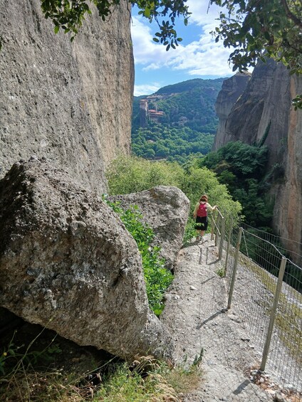 A person walking on a rocky path with a view of a valley and distant buildings. 3
