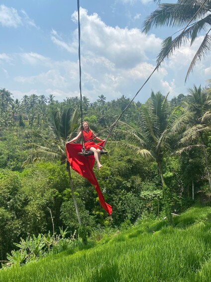 A person in a red dress swinging on a rope amidst lush greenery and palm trees. 5