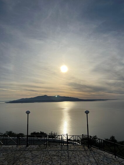 A sunset over a calm sea with a distant island, stone pathway, and two street lamps. 4