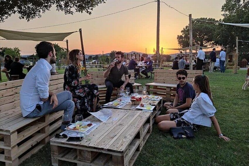 People sitting at wooden tables outdoors during sunset. 1