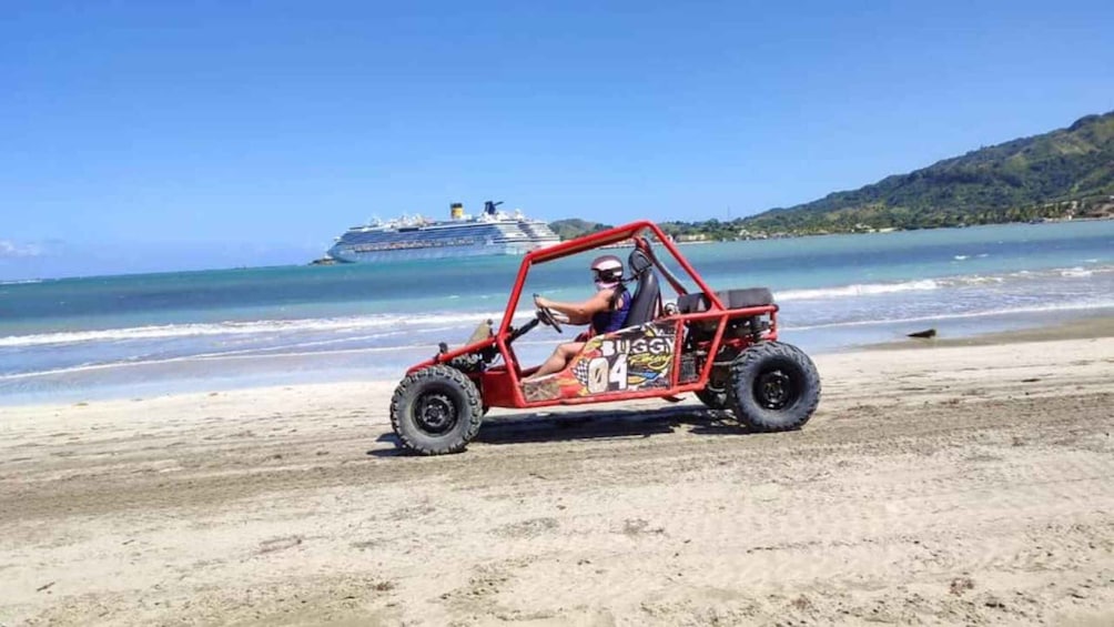 A red buggy with the number 04 on a sandy beach with a cruise ship in the background. 4