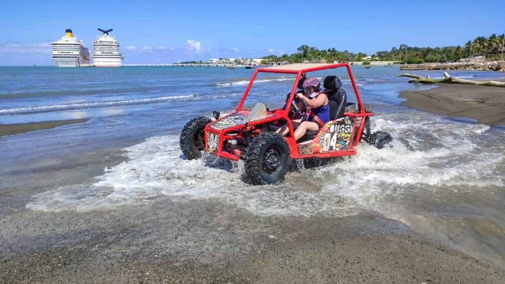 A red off-road vehicle on a beach with waves. 1
