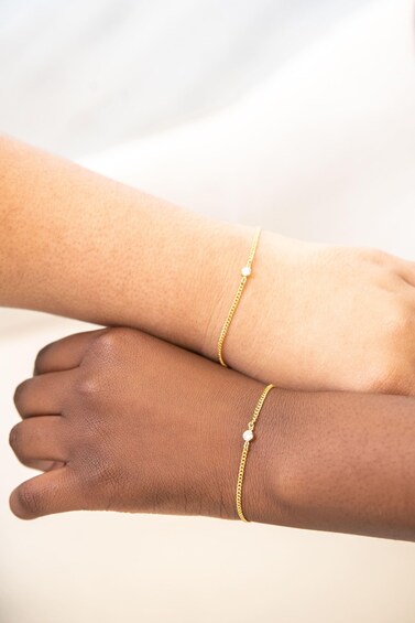 Two hands wearing gold bracelets with small pendants. 2