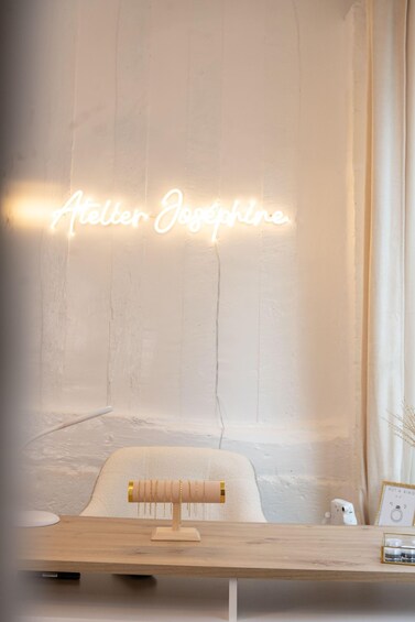 A wooden table with a neon sign reading "Atelier Jasmine" and a framed picture on the wall. 4