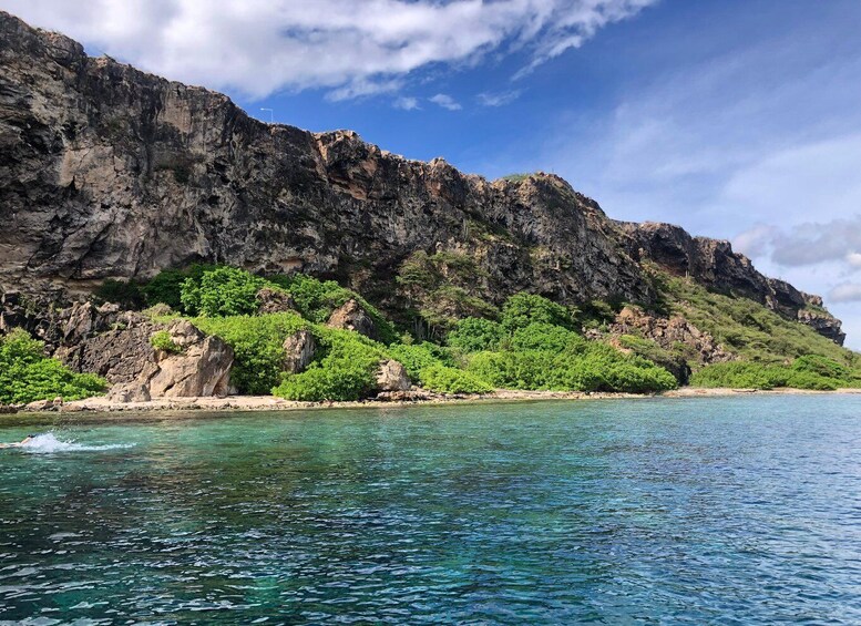 A coastal landscape with clear blue waters, rocky cliffs, and lush greenery. 2