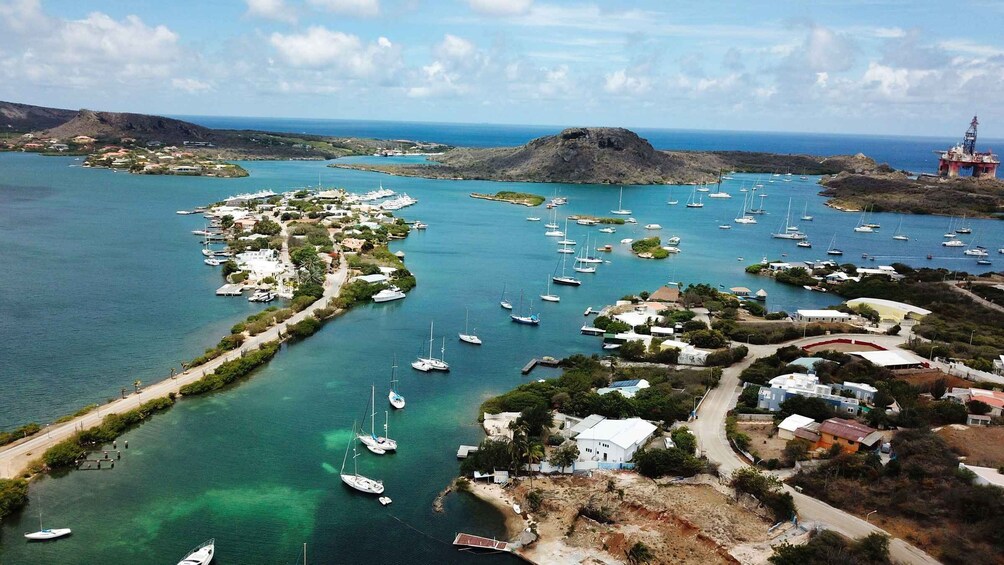 A coastal town with a marina filled with sailboats, surrounded by lush greenery and rocky terrain. 1
