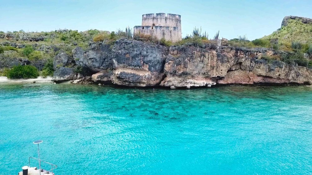 A coastal landscape with clear turquoise waters, a rocky cliff, and a circular stone structure on top. 3
