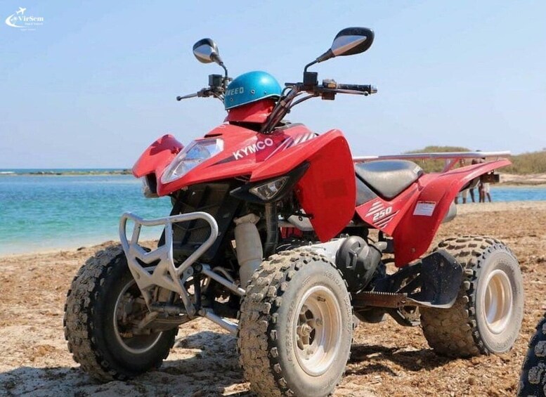 A red ATV with 'KYMCO' and '250' on it, parked on a sandy beach with water in the background. 3