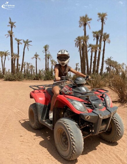 A person riding a red ATV on a dirt path with palm trees in the background. 1