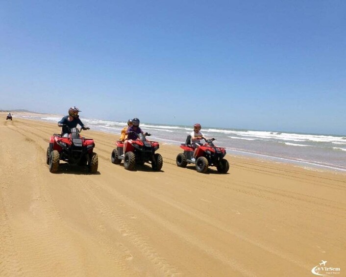 Three people riding red ATVs on a sandy beach with the ocean in the background. 4