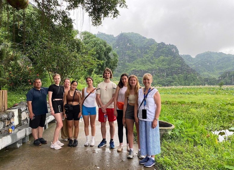 A group of people standing on a wet path with a lush green landscape and mountains in the background. 3