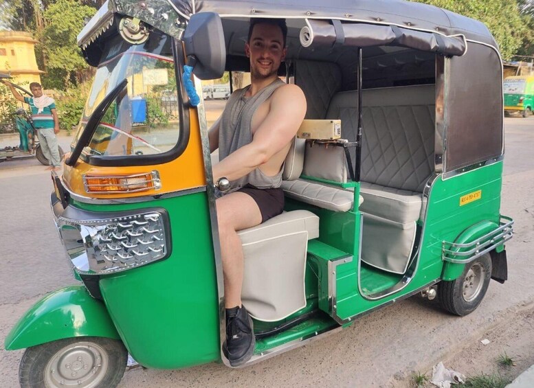 A man sitting in a green and yellow auto-rickshaw. 1