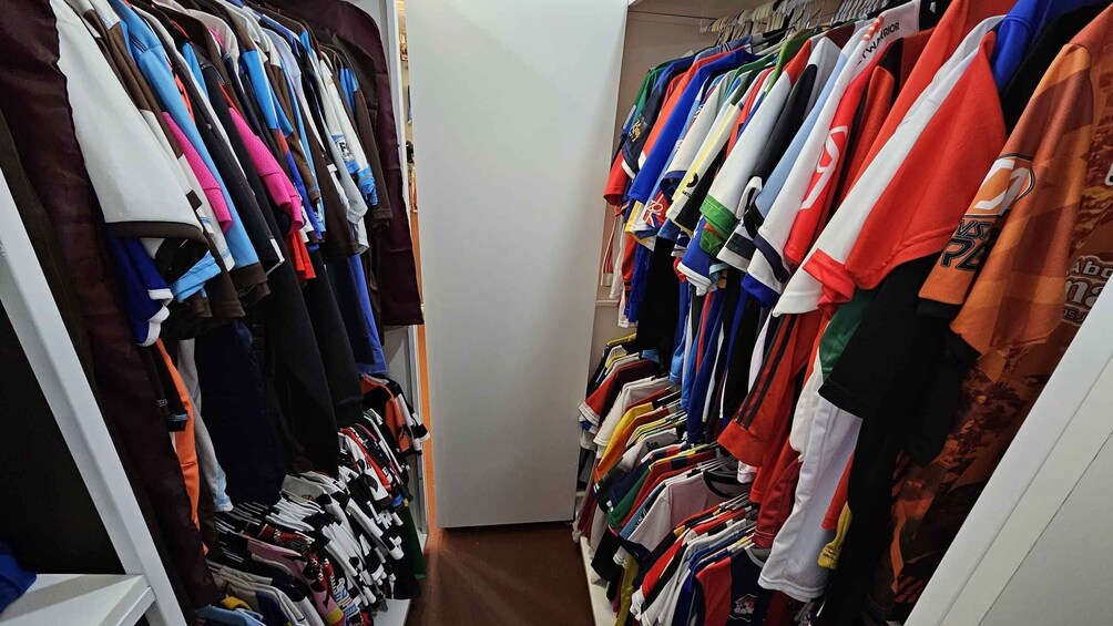 A narrow walk-through closet with various sports jerseys and shirts hanging on racks. 2