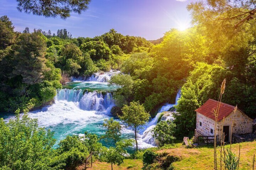 Une cascade se jetant dans une rivière, le tout entouré d’une végétation luxuriante et d’un petit bâtiment en pierre. 3