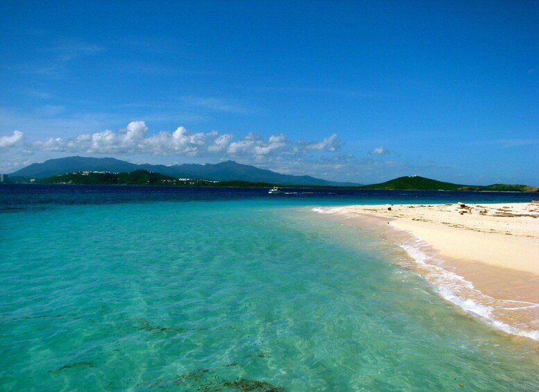 A beach with clear turquoise water, a sandy shore, and distant mountains under a blue sky. 5