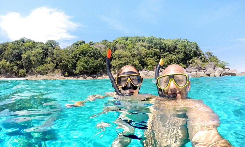Two people snorkeling in clear blue water with a forested island in the background. 3