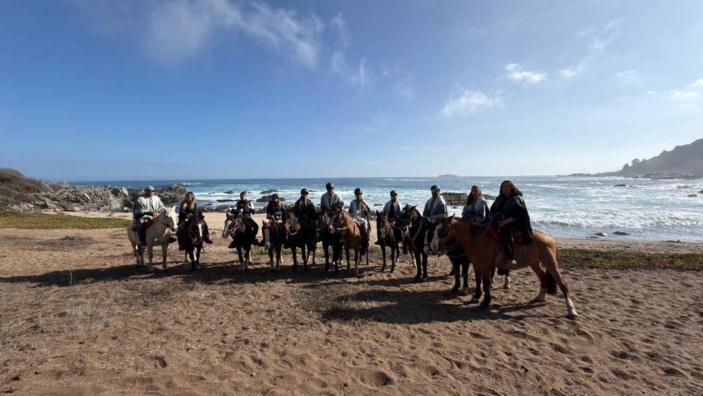 A group of people riding horses on a beach with the ocean in the background. 3