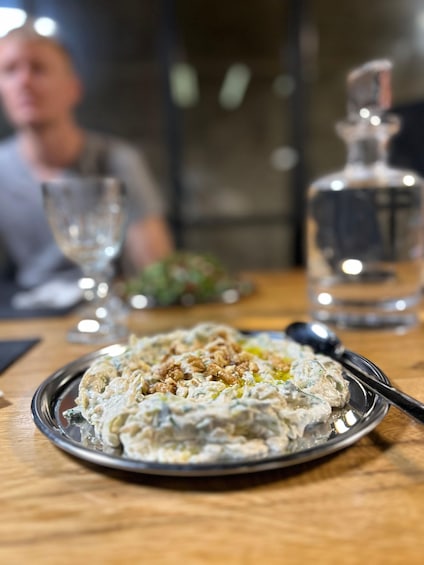 A plate of food with a creamy texture, garnished with nuts, on a wooden table. 1
