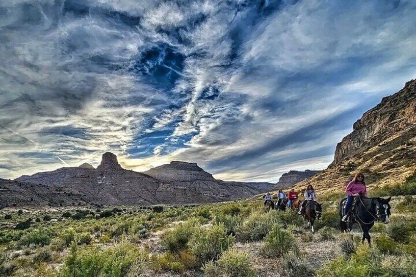 A group of people horseback riding in a desert landscape with mountains in the background. 3