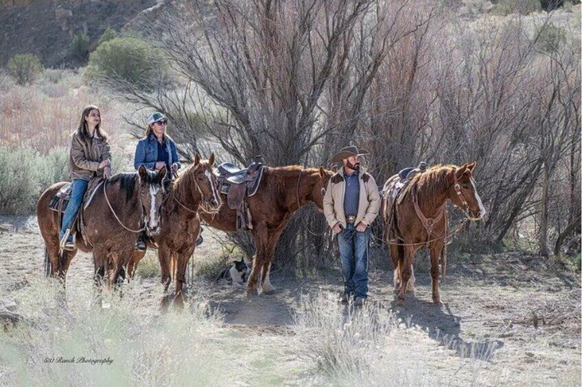 Tres personas a caballo en un campo seco y cubierto de hierba, con árboles dispersos al fondo. 2