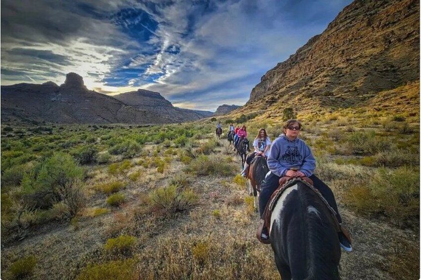 Un grupo de personas cabalgando por un paisaje desértico con colinas rocosas y vegetación escasa. 1