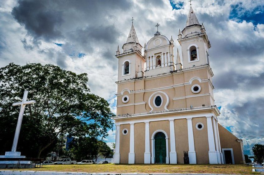 A church with three towers and a large cross in front. 1