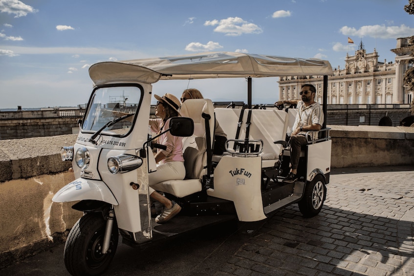 A tuk-tuk parked on a cobblestone path with a historic building in the background. 1