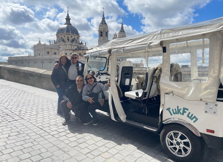 A group of people posing in front of a white tuk-tuk with 'TukFun' branding parked on a cobblestone path. 5