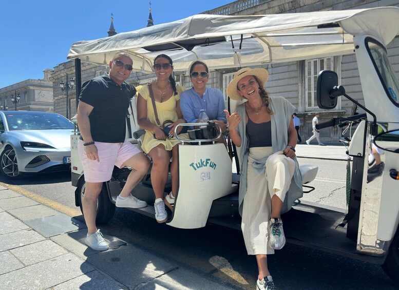 Four people on a white vehicle with 'TakFun' branding, parked on a city street with buildings and a car in the background. 1