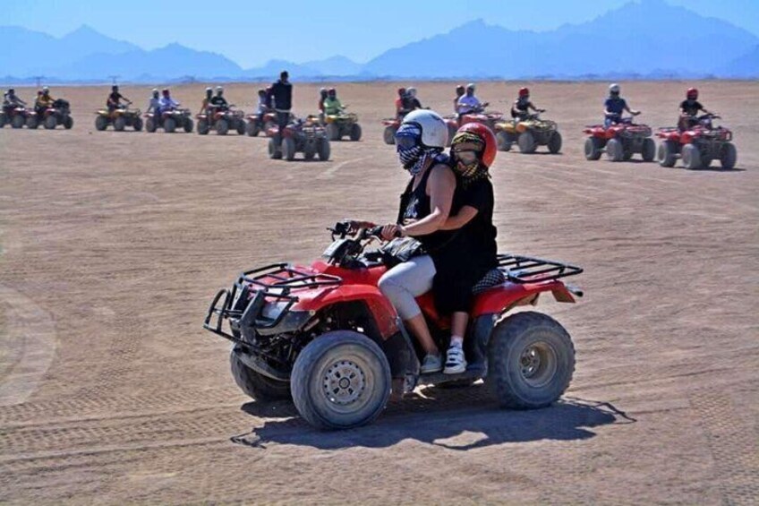 Un gruppo di persone che guidano quad attraverso un terreno pianeggiante e aperto, con montagne sullo sfondo. 5