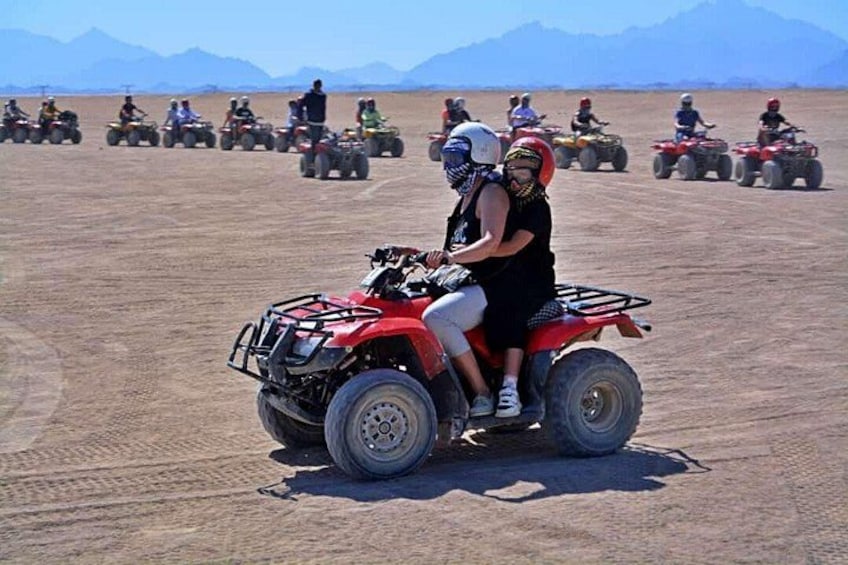 Eine Gruppe von Personen fährt mit Quads durch eine Wüstenlandschaft, im Hintergrund sind Berge zu sehen. 4