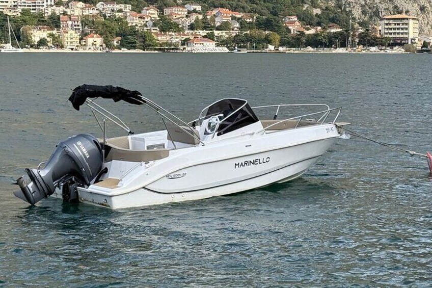 A white motorboat named MARINELLO on calm water with a cityscape in the background. 1