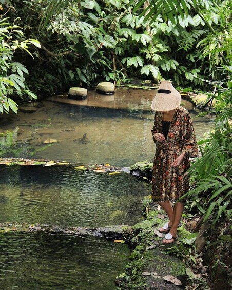 A person standing on rocks by a clear stream in a lush, green environment. 2