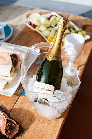 A bottle of champagne in a clear ice bucket on a wooden table. 2